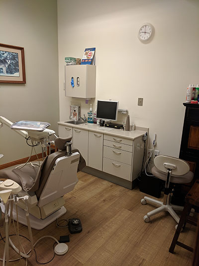 The image depicts a dental office interior with various pieces of equipment visible, including a dental chair, dental equipment, and a reception desk.