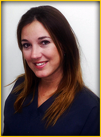The image features a woman wearing a blue shirt and a dark-colored blazer, with her hair styled down, smiling at the camera.
